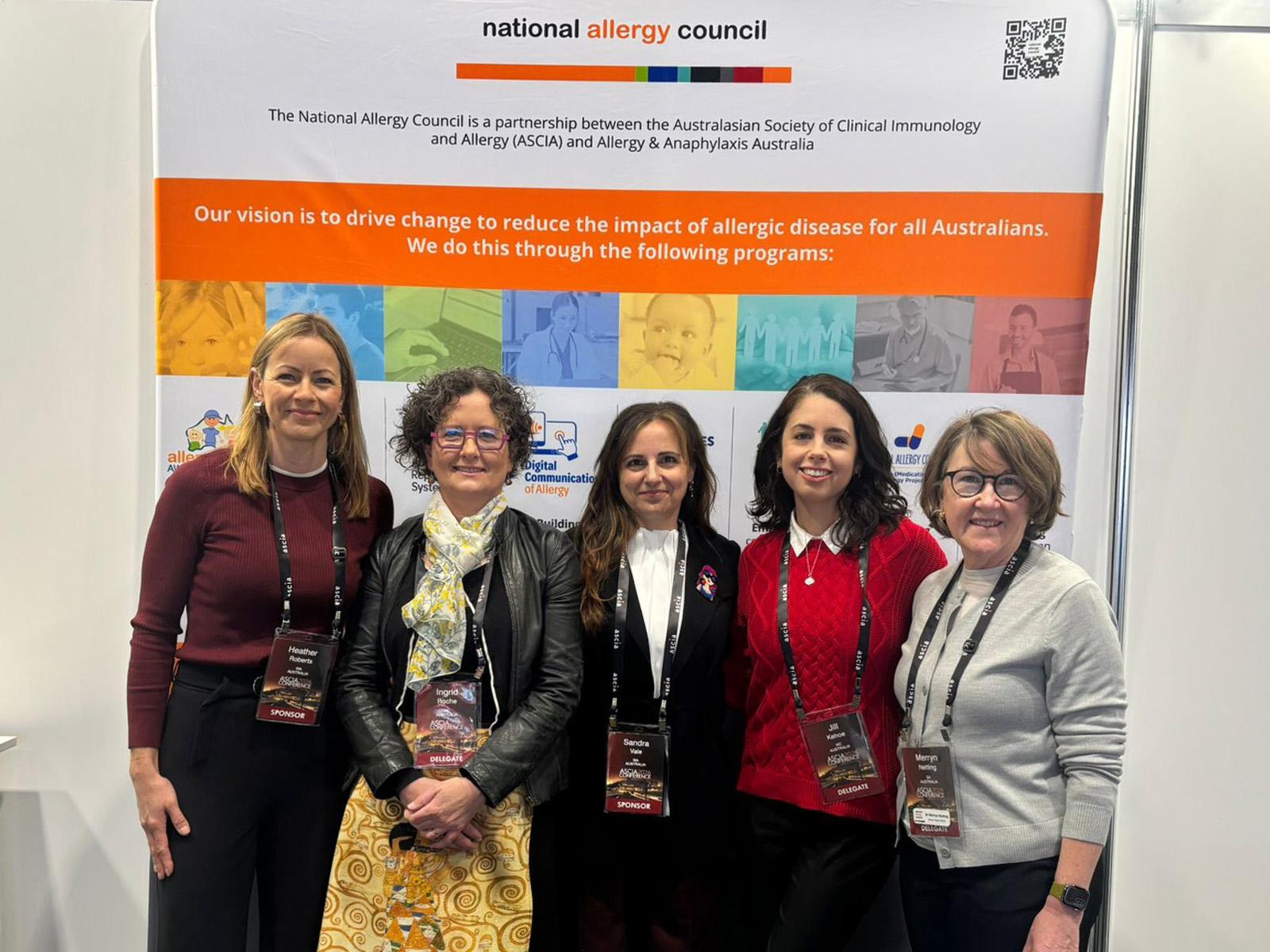 Five women standing together in front of a National Allergy Council banner, smiling at the camera.