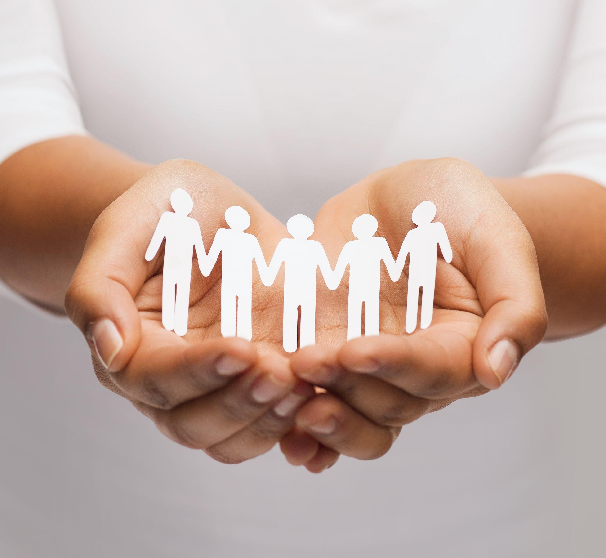 Hands gently holding paper cutouts of five people linked together, symbolizing unity and support.