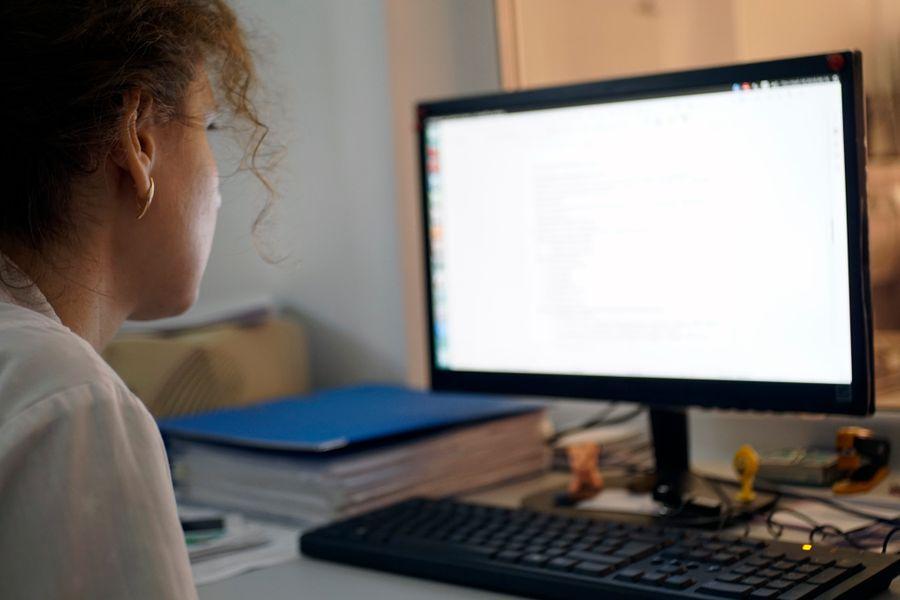 A person with curly hair working on a computer at a desk, focusing on the screen.