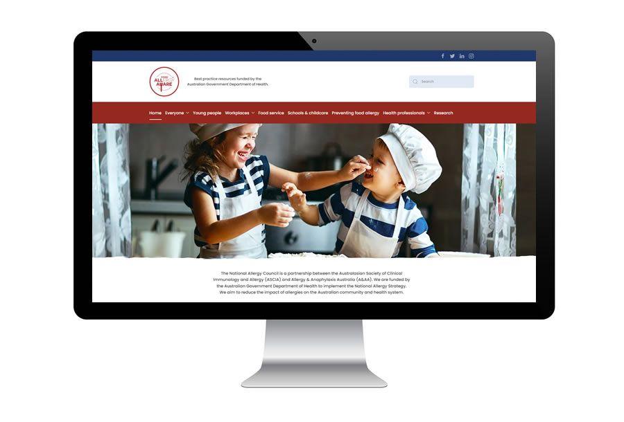 Website for Food Allergy aware with a banner showing two children in chef hats and aprons playfully interact in a kitchen setting, displayed on a computer monitor.